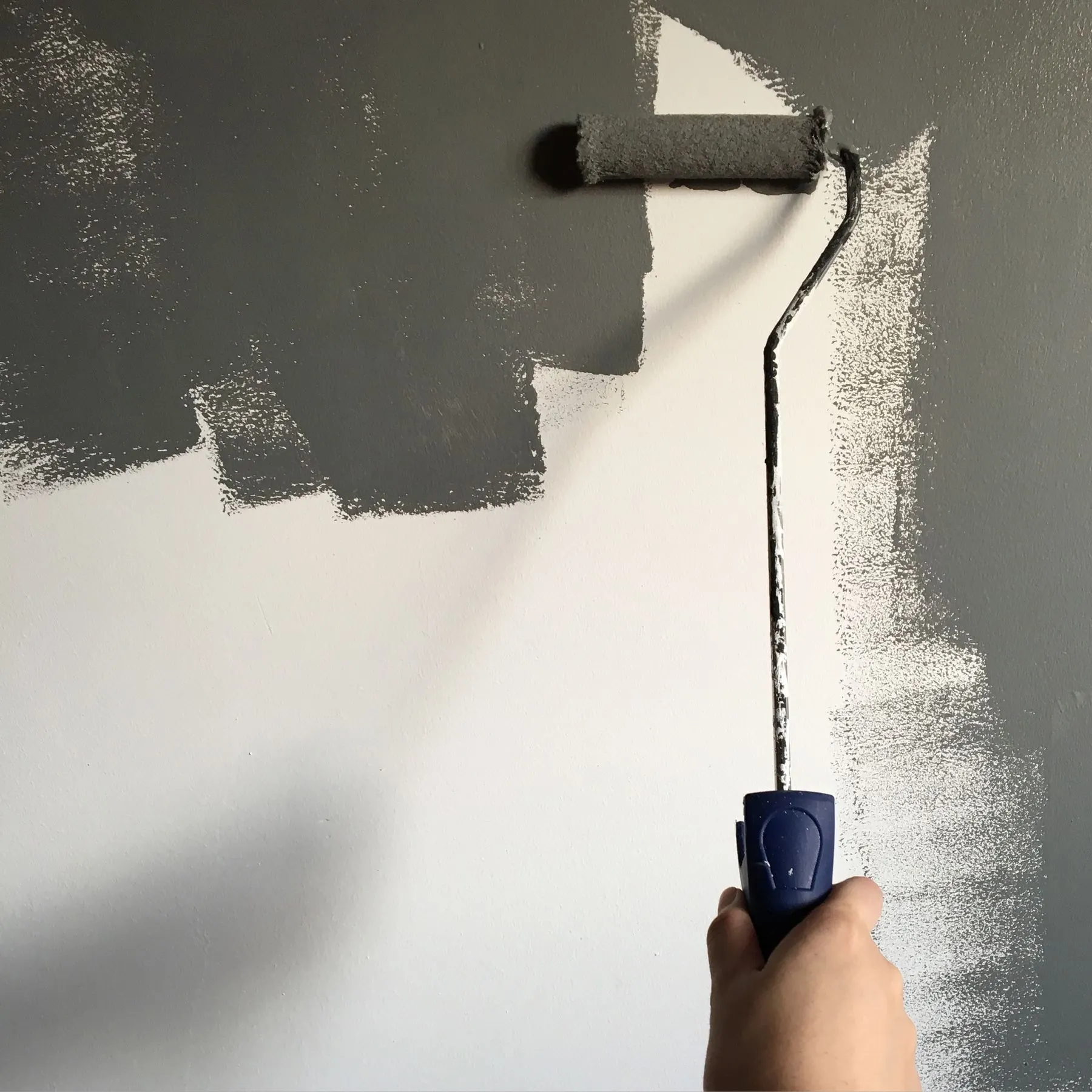 Paint roller applying a dark gray coat to an interior wall